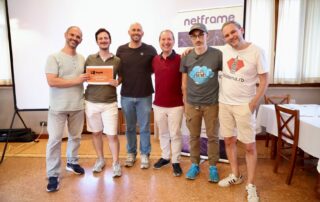 Foto di gruppo alla serata Modena Full Stack sulla migrazione DNS in cloud: lo speaker Andrea Carratta e le community tech modenesi davanti al roll-up Netframe