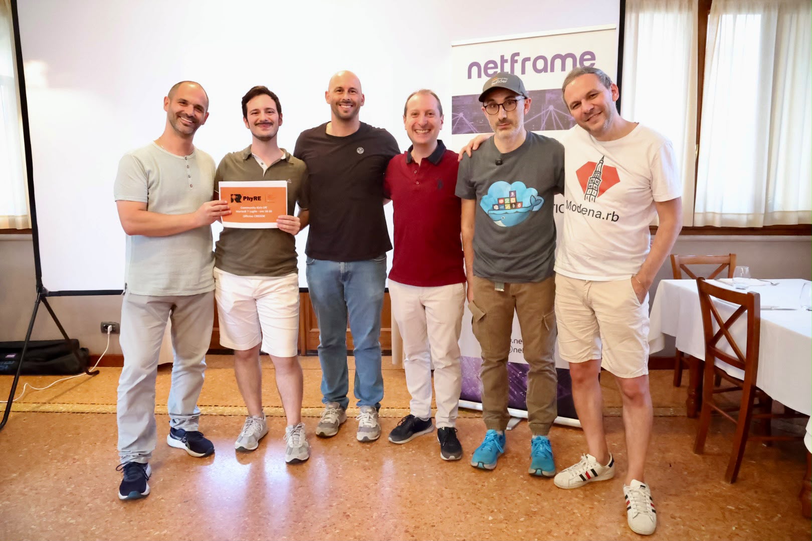 Foto di gruppo alla serata Modena Full Stack sulla migrazione DNS in cloud: lo speaker Andrea Carratta e le community tech modenesi davanti al roll-up Netframe