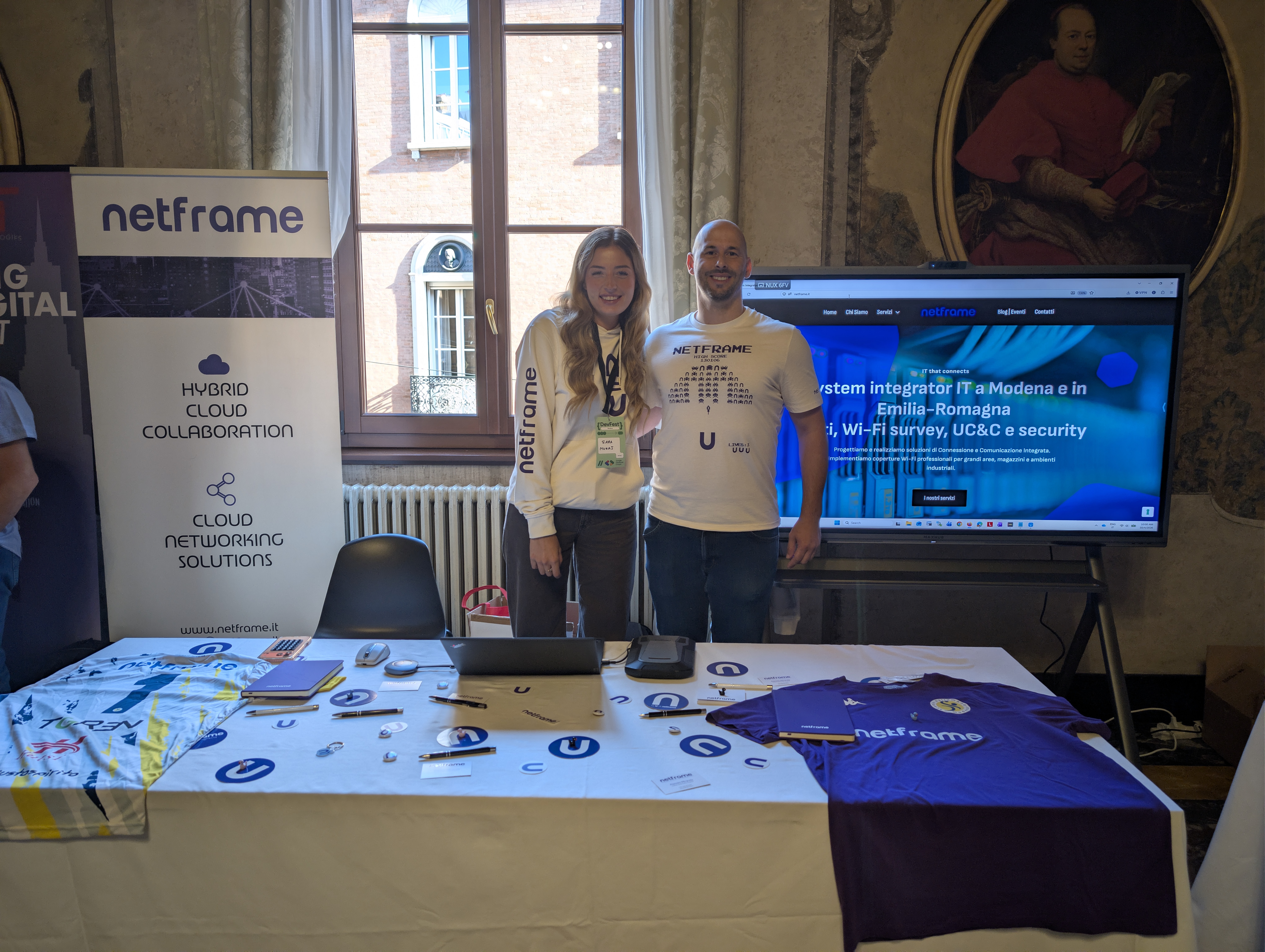 Stand Netframe al DevFest Modena 2026 nella Fondazione Collegio San Carlo, con l'analizzatore di spettro Wi-Fi Ekahau e il monitor interattivo MaxHub XBoard V7 da 65 pollici